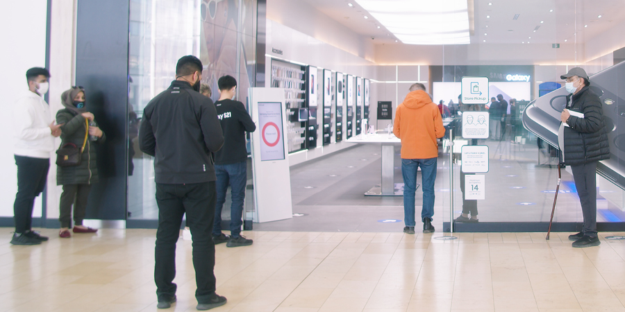 Customers wearing masks wait outside the Samsung Experience Store at Yorkdale Shopping Centre. Melitron's People Count Kiosk at the entrance displays 